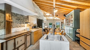 A modern kitchen with a central island, wooden ceiling beams, and a stone accent wall.