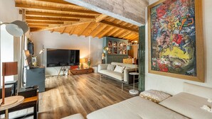 A spacious living room with wooden beams, a large abstract painting, and a cozy sofa.