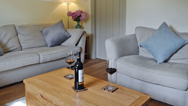 A living room with two grey sofas, a wooden coffee table, a wine bottle, and a glass of red wine. - 2 bedroom accommodation in Fordwich, Canterbury (Fordwich, Canterbury)