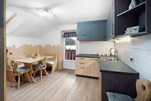 Una cocina con armarios de madera, una mesa de comedor con sillas, un ventanal con vista a árboles y un lavamanos empotrado.