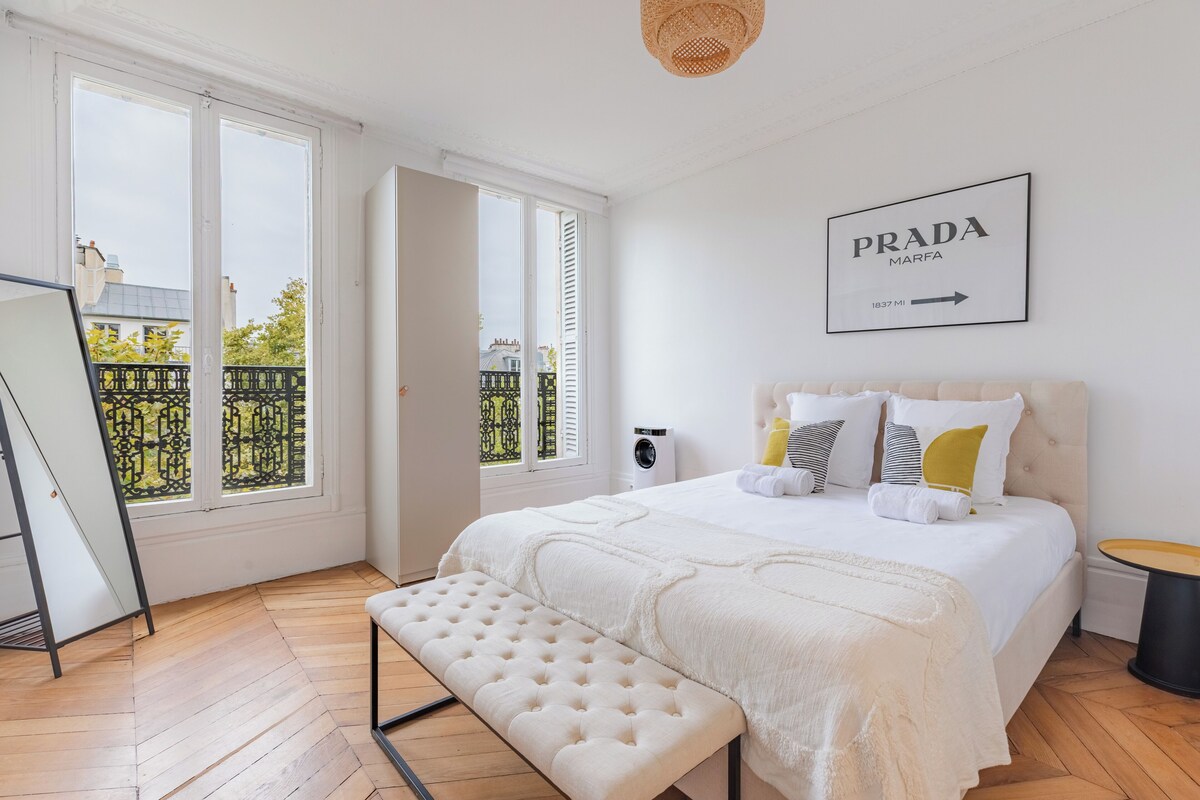 Une chambre avec un grand lit, un banc, une fenêtre donnant sur un beau paysage et un panneau fixé au mur.