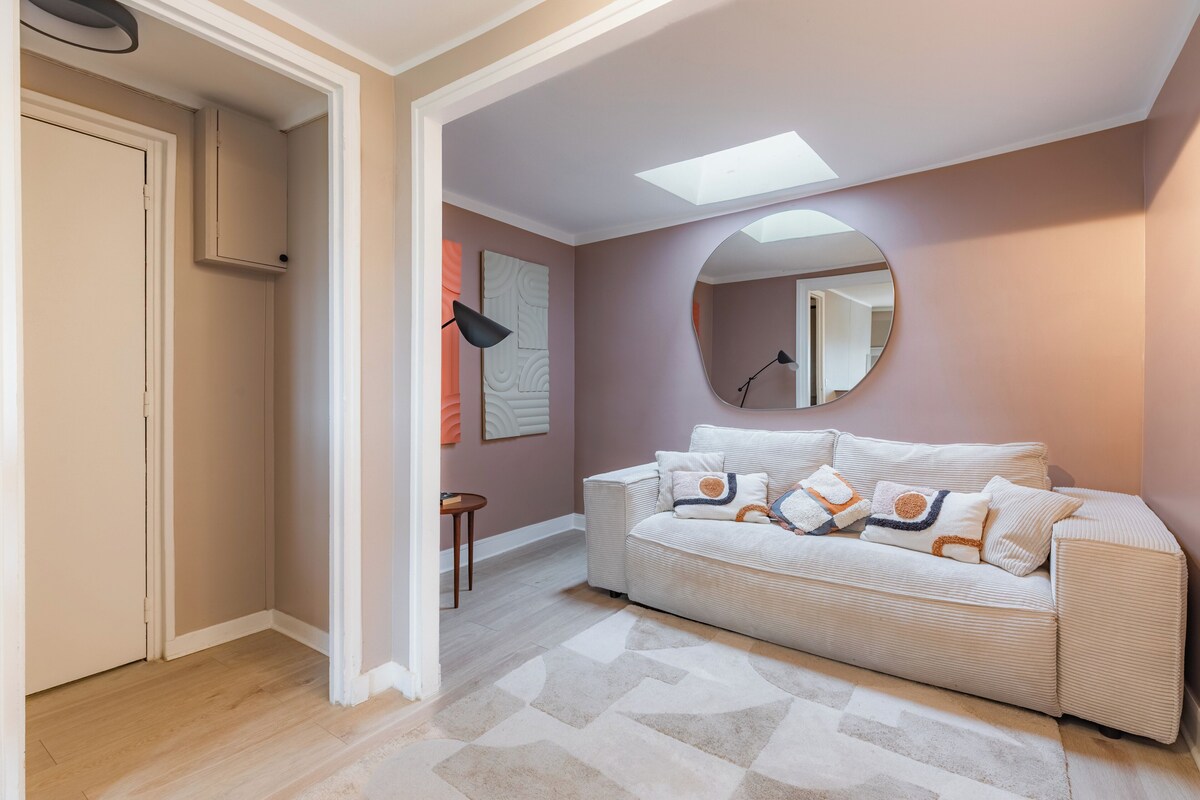Un salon moderne avec un canapé beige, un miroir rond et un tapis à motifs géométriques.