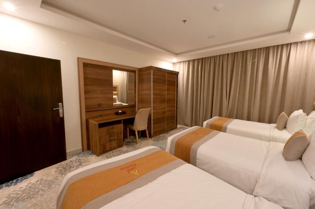 Habitación de hotel con dos camas, un escritorio, una silla, un armario y un gran ventanal con cortinas.