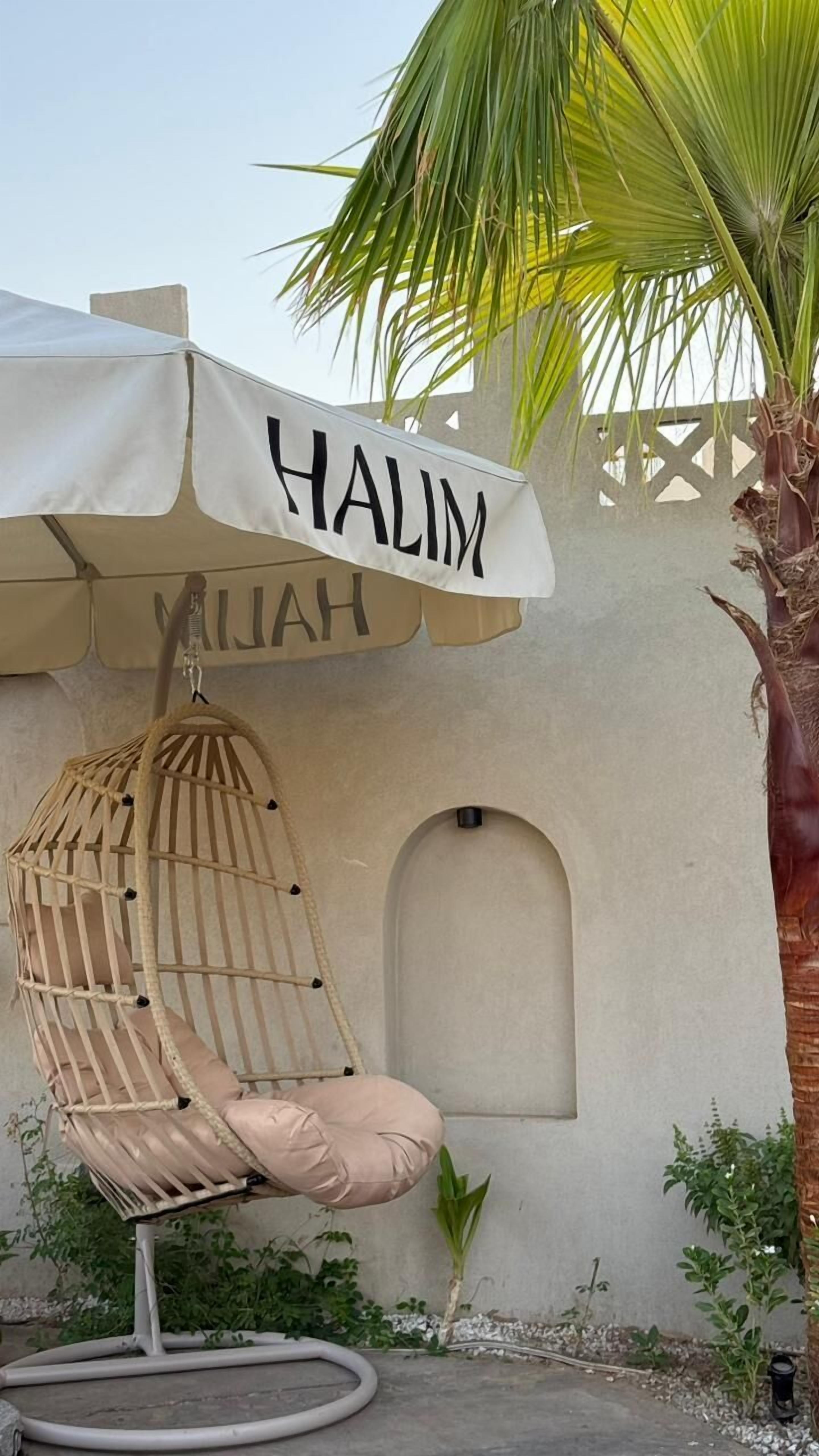 Una silla colgante con dosel, con la etiqueta 'HALIM' y una pequeña ventana en forma de arco en la fachada de un edificio.