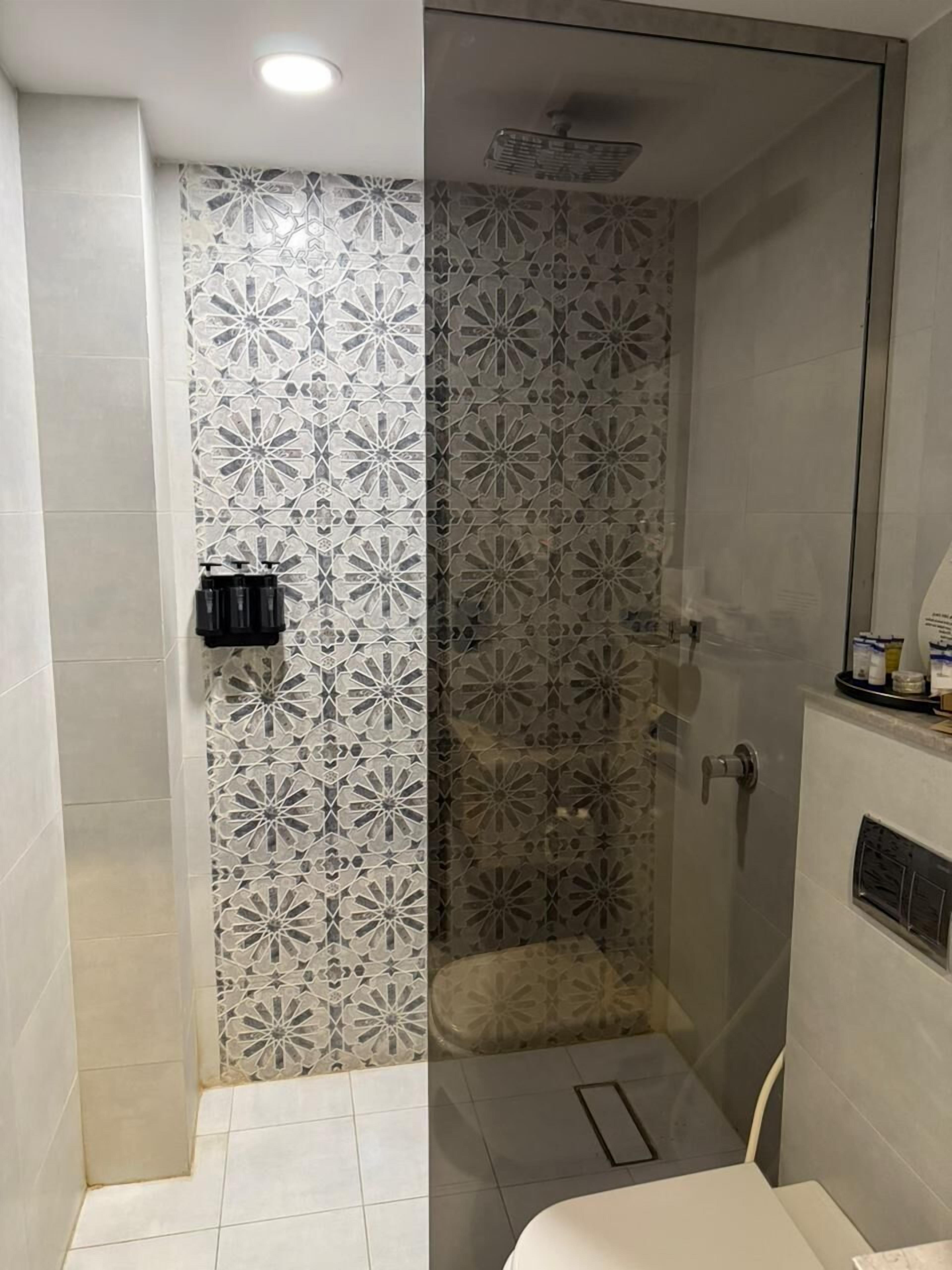 Een douche met een glazen deur, betegelde wanden en een klein plankje met toiletartikelen.