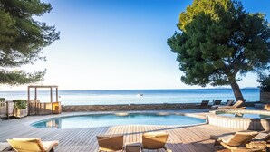 Une terrasse en bois avec des chaises longues et une piscine donnant sur la mer.