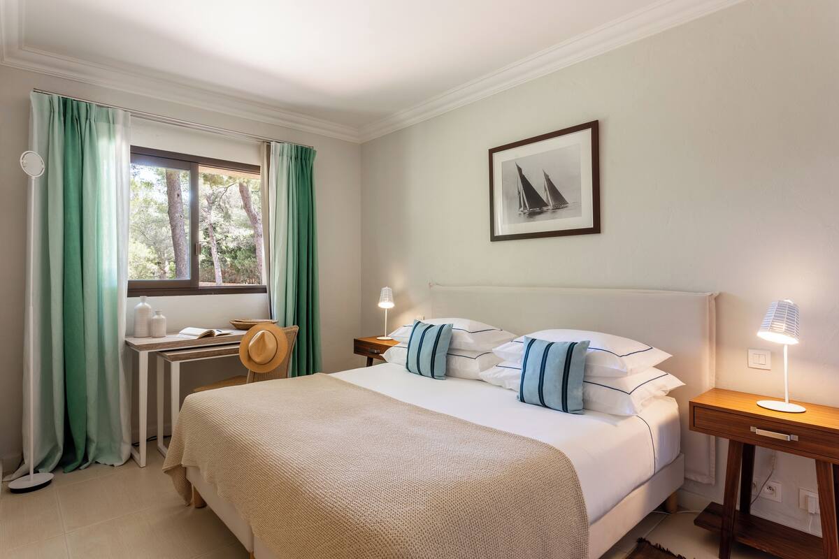 Habitación de hotel ordenada con cama, escritorio, silla y ventana con cortinas.