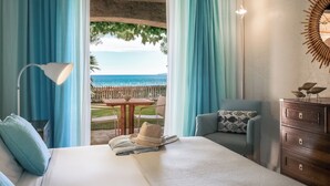 Une chambre d’hôtel comprenant un lit, un bureau, une chaise, une commode et une vue sur la mer grâce à de grandes fenêtres.