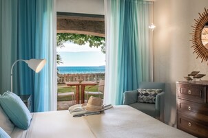 Habitación de hotel con cama, escritorio, silla, cómoda y vistas al mar a través de amplias ventanas.