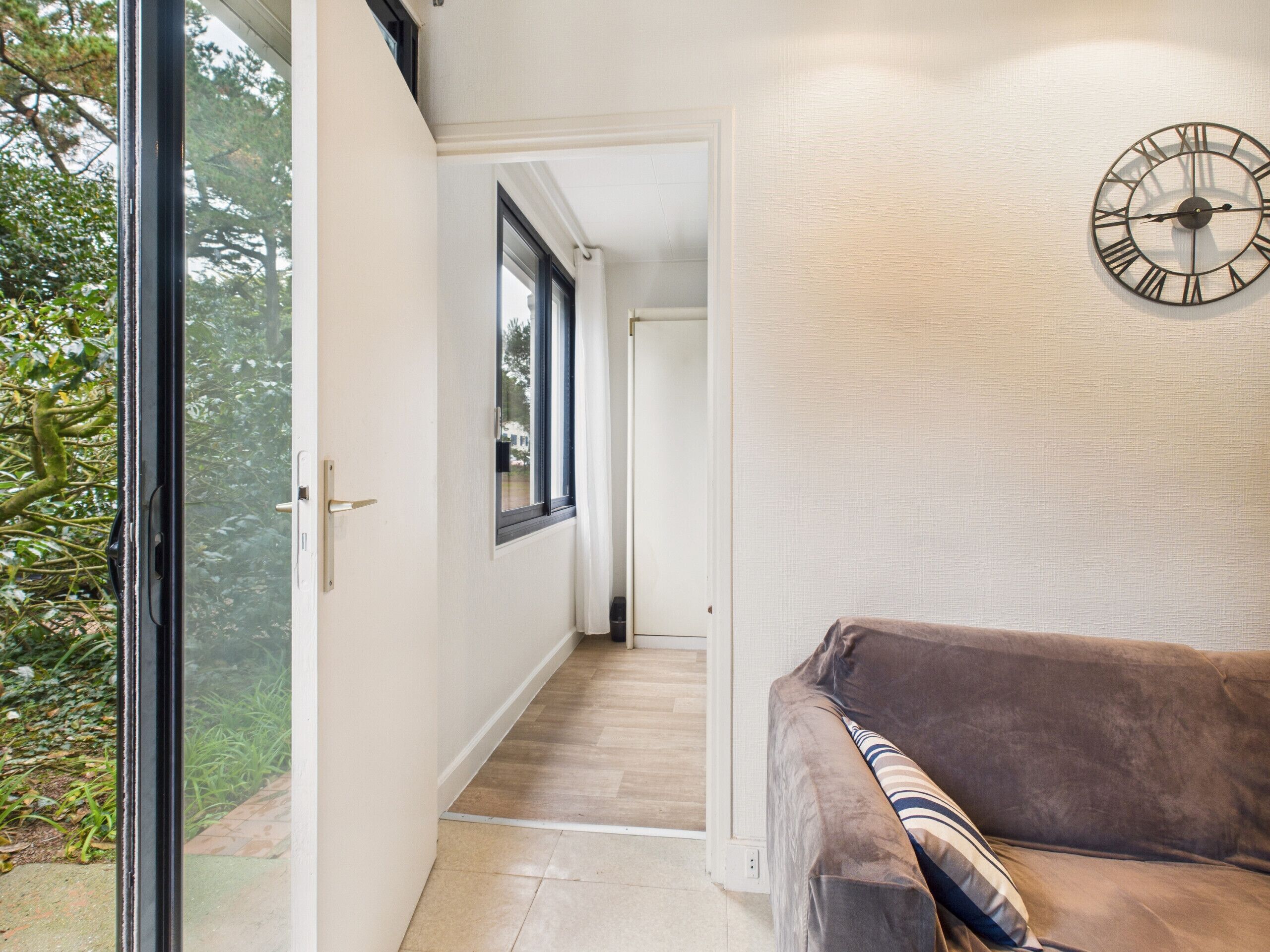 A hallway with a view of a garden, a door, and a clock on the wall.