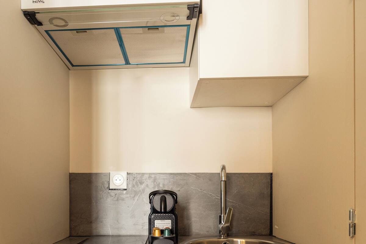 Una cucina compatta con lavastoviglie integrata, lavello in acciaio inossidabile, macchina da caffè e cappa aspirante moderna.