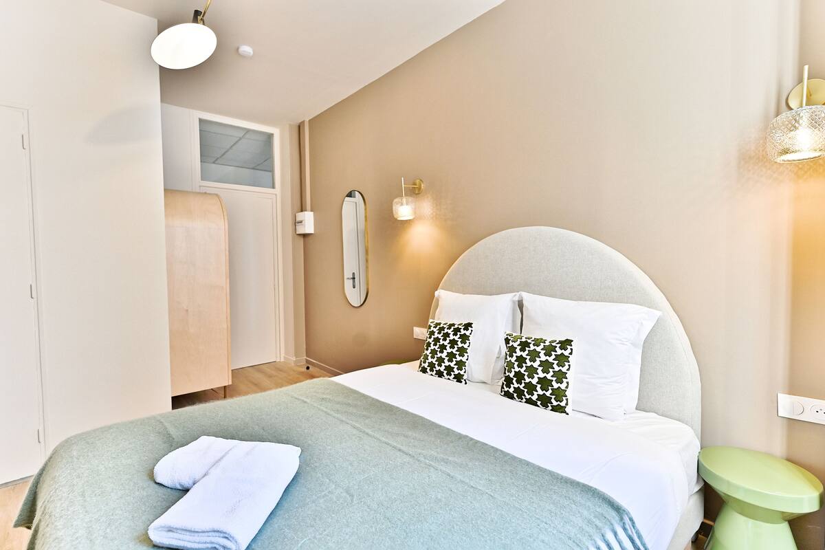 Una camera da letto moderna con un letto grande, una parete verde a contrasto e un piccolo sgabello verde.