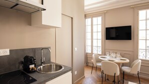 Une cuisine moderne équipée d’un four encastré, d’un évier et d’une machine à café. On y trouve également un coin repas avec une table ronde et quatre chaises. Un téléviseur à écran plat est fixé au mur, au-dessus de la table à manger.