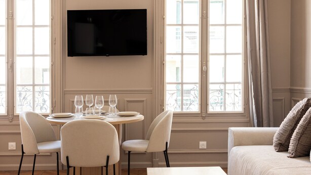 Une chambre d’hôtel moderne dotée d’une grande fenêtre, d’un téléviseur à écran plat, d’une table à manger avec des chaises et d’un canapé.