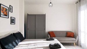 A bedroom with a bed, a grey sofa, a wardrobe, and framed pictures on the wall.