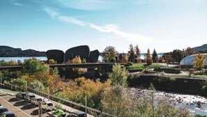 A modern building with a unique architectural design, a parking area, and a river with a bridge in the background.