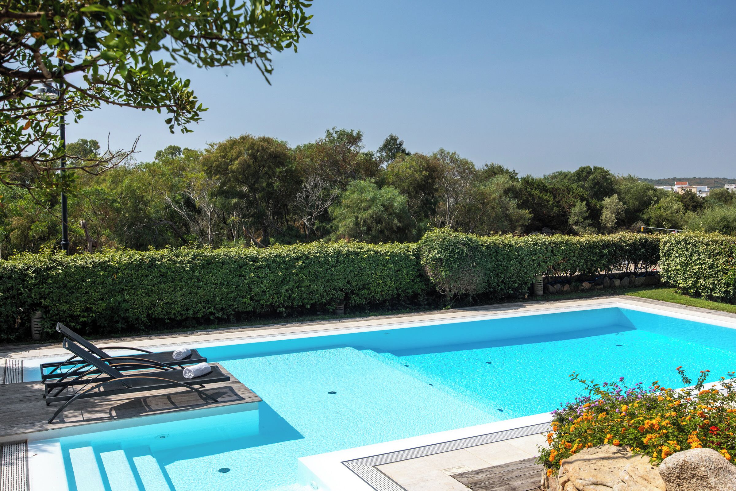 A rectangular swimming pool with clear blue water, surrounded by a wooden deck and lounge chairs.