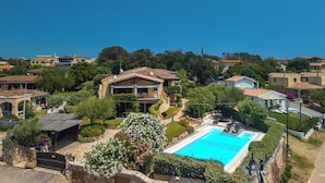 Un quartier résidentiel doté d’une piscine, entouré d’une végétation luxuriante et de maisons à l’architecture méditerranéenne.