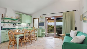 Un espace de vie compact comprenant un coin repas, une kitchenette et un canapé vert.