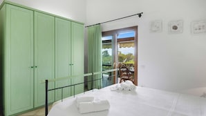 Une chambre avec un lit, une armoire verte, un balcon avec une table et des chaises, et une vue sur la verdure.