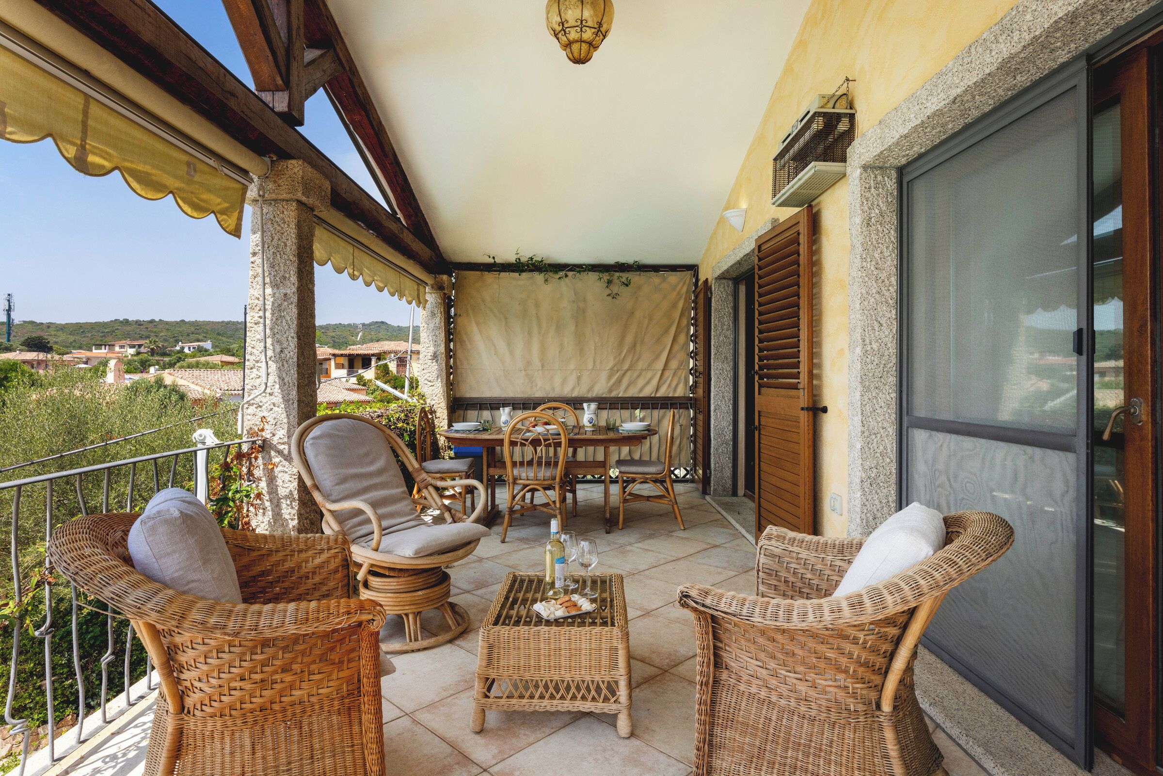 A balcony with wicker furniture, a table set for dining, and a view of the countryside.
