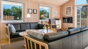 Ein modernes Wohnzimmer mit einem schwarzen Ledersofa, einem runden Couchtisch und einem an der Wand befestigten Fernseher.