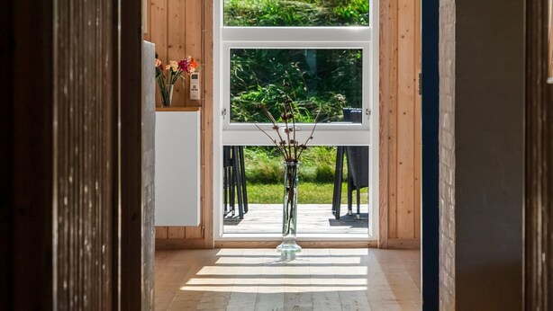 Ein Holzinterieur mit einem großen Fenster, einer Vase mit Blumen und Blick ins Grüne.