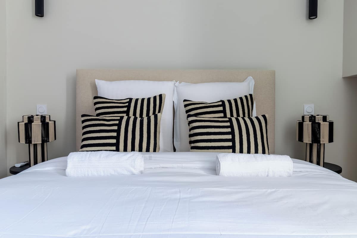 A neatly made bed with white linens and striped pillows, flanked by two bedside tables with lamps.