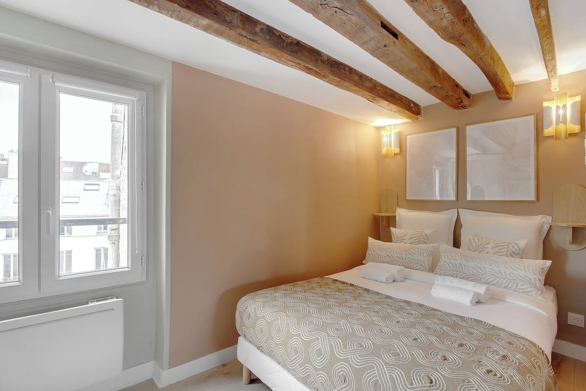 A bedroom with a large bed, a window, and exposed wooden beams on the ceiling.