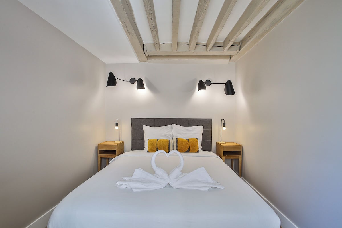 A hotel room with a neatly made bed, two bedside tables, a headboard, and wall-mounted lighting.