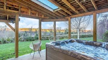 Un jacuzzi bajo una pérgola de madera con vistas a un paisaje cubierto de césped.