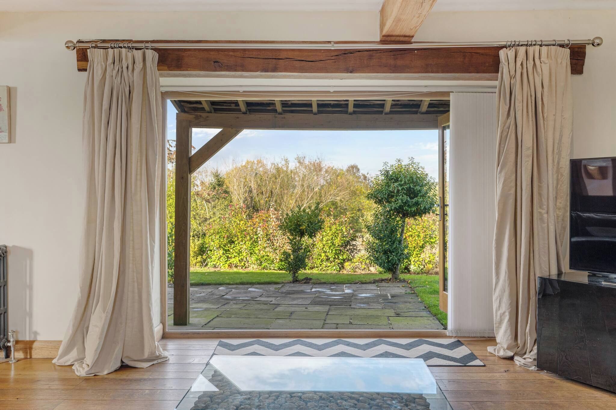 Una habitación con techo de madera, cortinas color beige, un sendero de piedra que conduce al exterior y un televisor sobre un mueble.