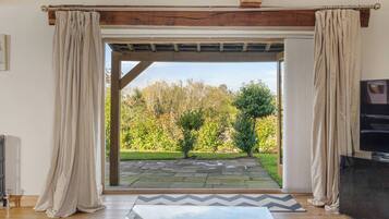 Una habitación con techo de madera, cortinas color beige, un sendero de piedra que conduce al exterior y un televisor sobre un mueble.