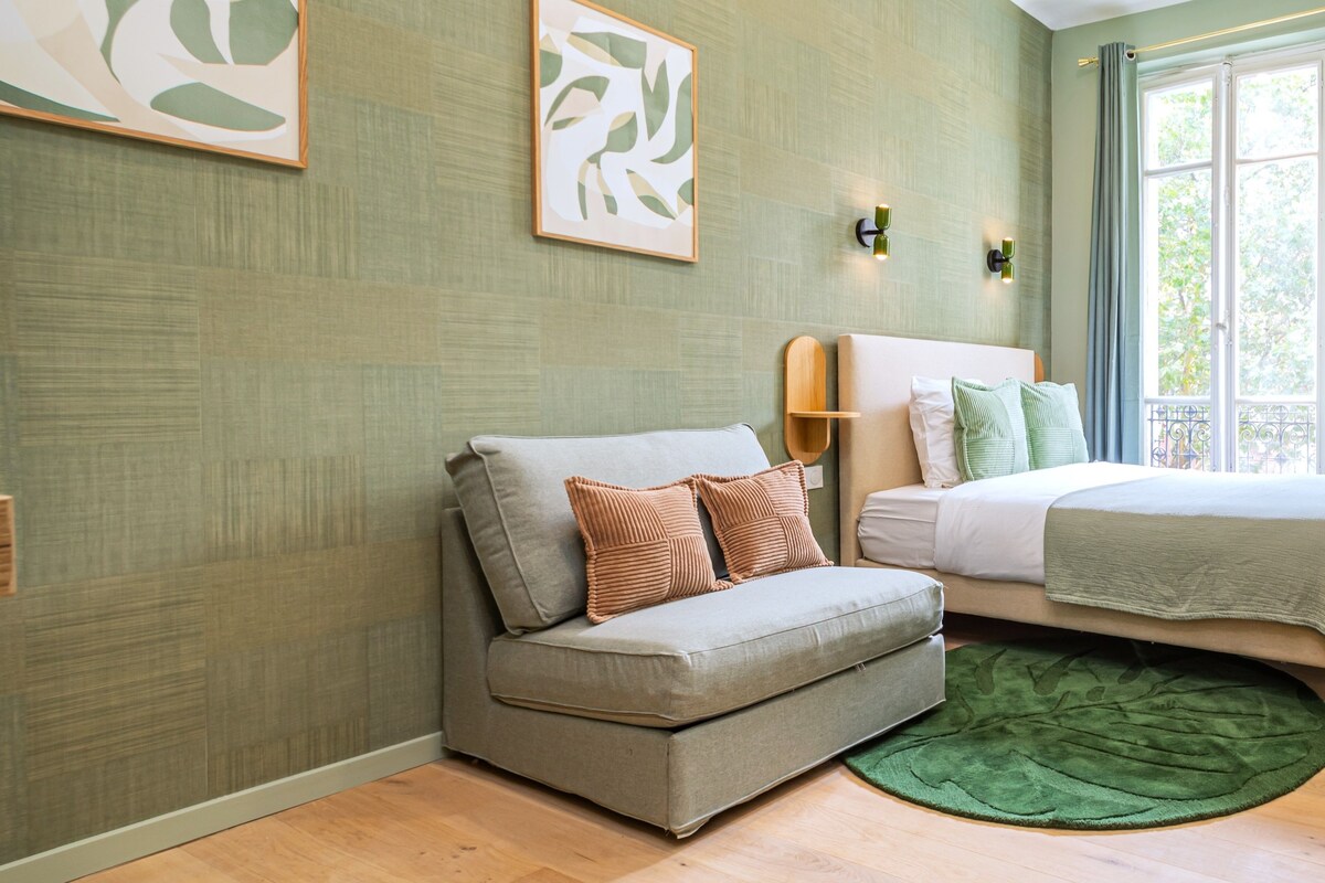 Un dormitorio moderno con un sofá gris, una cama con ropa de cama blanca y un cuadro abstracto de color verde en la pared.