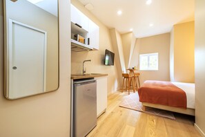 Ein kleines Zimmer mit Küchenzeile, einem Bett, einem Fernseher und einem Fenster.