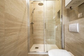 Ein modernes Badezimmer mit einer gläsernen Duschkabine, einer weißen Toilette und einer Wand mit Marmorfliesen.