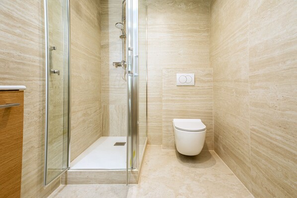 A modern bathroom with a glass shower enclosure, a toilet, and a wooden vanity. - Apparements Berthier (Paris)