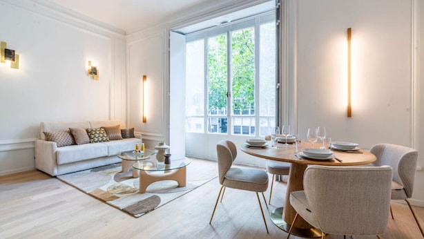 A modern living room with a sofa, coffee table, and dining area with chairs and a table set for dining. - Apparements Berthier (Paris)