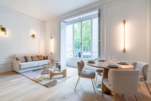 A modern living room with a sofa, coffee table, and dining area with chairs and a table set for dining. - Apparements Berthier (Paris)