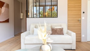 A modern living room with a white sofa, a glass coffee table, and a vase with dried plants. - Apparements Berthier (Paris)