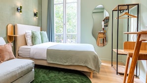 A bedroom with a bed, a chair, a desk, a mirror, and a window with curtains. - Apparements Berthier (Paris)