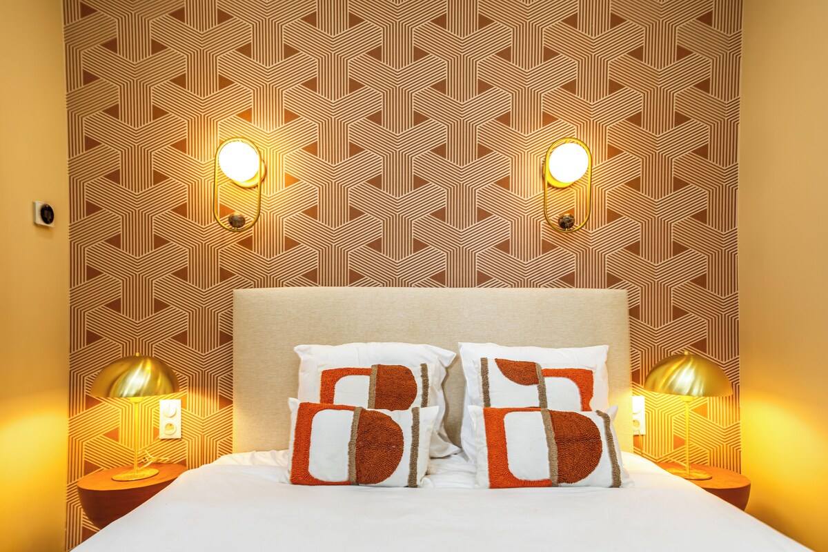 Una habitación de hotel con papel tapiz estampado, dos lámparas de noche y una cama con almohadas.