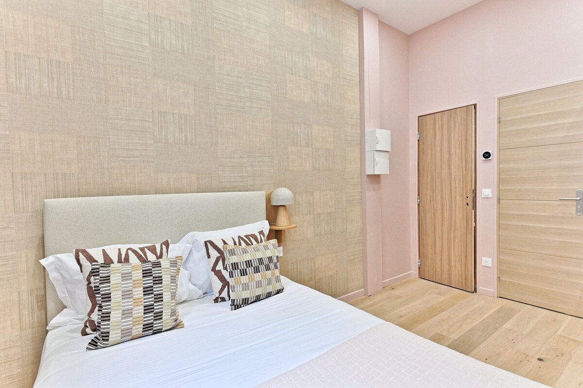 Un dormitorio con una cama, almohadas, una mesita de noche con lámpara y un armario de madera.