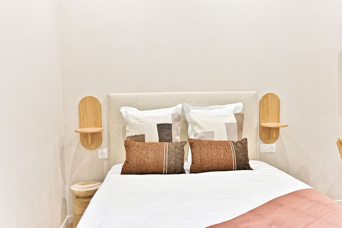 Una cama bien hecha con edredón blanco, dos almohadas marrones y cabecero de madera.