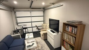 A compact living space with a sofa, a coffee table, a TV, a bookshelf, and a radiator. - A private mini house with own T&B, mini kitchen and entertainment area! (Dunedin)