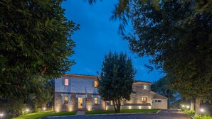 A stone building with a well-maintained lawn and gravel driveway, surrounded by trees. - Villa ai Caprioli Mondaino (Emilia-Romagna)
