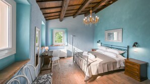 A bedroom with a wooden ceiling, a bed with white linens, a desk with a chair, and a window with a view of greenery. - Villa ai Caprioli Mondaino (Emilia-Romagna)