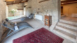 A room with a stone wall, a pool, and a massage chair. - Villa ai Caprioli Mondaino (Emilia-Romagna)