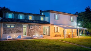 A two-story house with a stone facade, a covered patio with outdoor seating, and a well-maintained lawn. - Villa ai Caprioli Mondaino (Emilia-Romagna)