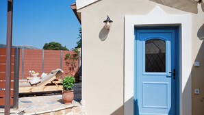 A beige building with a blue door, a small outdoor seating area with a lounge chair and potted plants, and a stone staircase leading to the entrance.